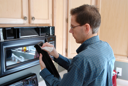 Man cleaning up after replacing the filter in a microwave in the kitchen of a modern home.