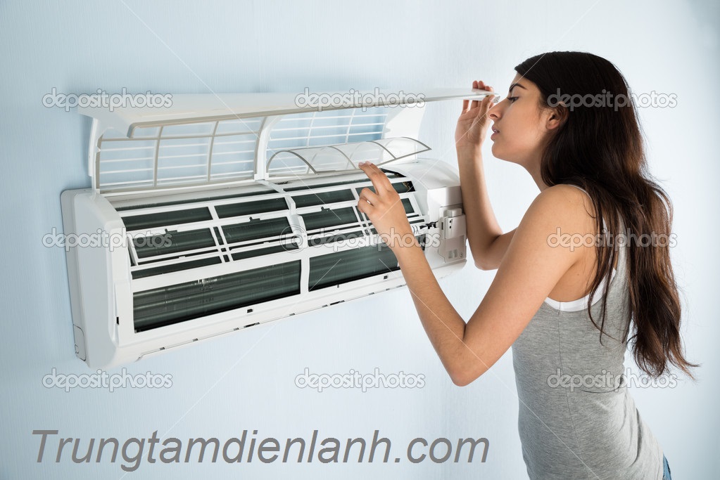 Young Woman Checking Air Conditioner In House